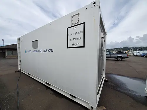 The white exterior of a portable lab van in front of a building.