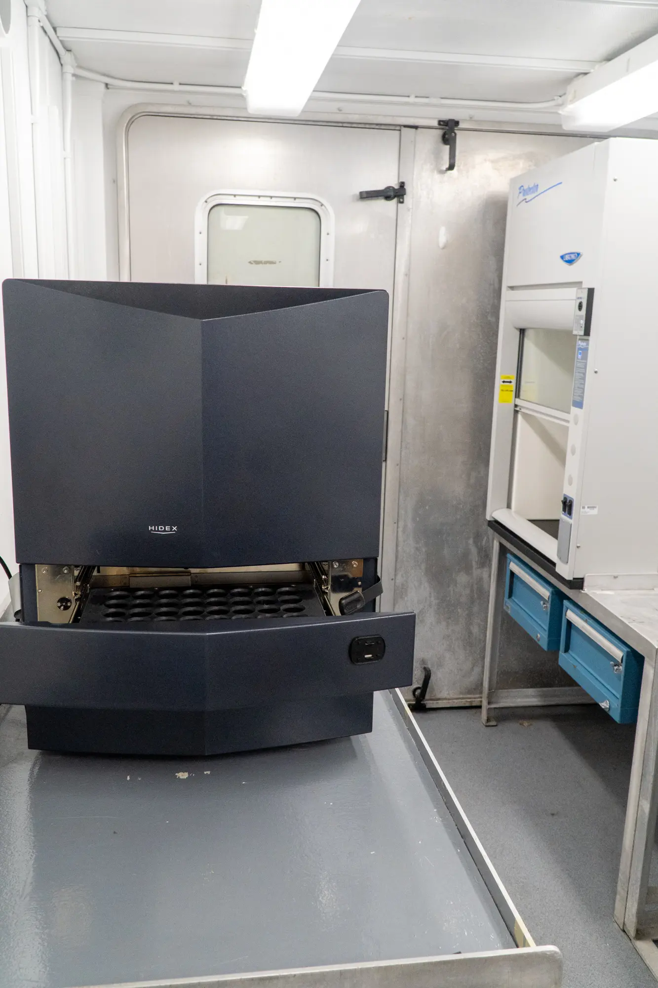 A black Hidex with its drawer open and a fume hood.