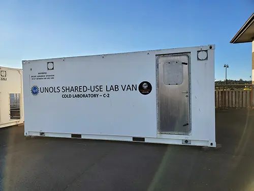 The white exterior of the side of a portable lab van showing a silver door.