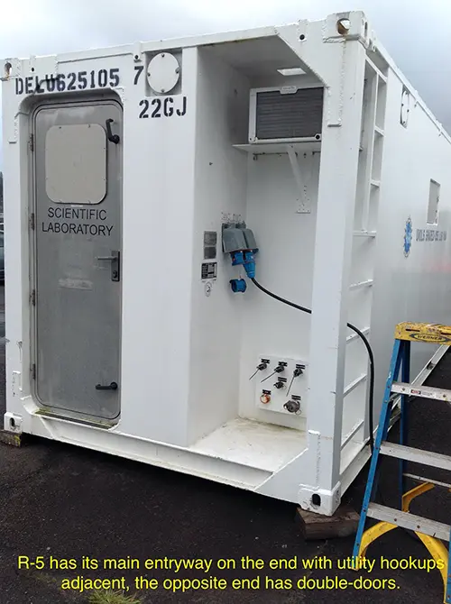 The white exterior of a portable lab van showing its main entry on the end with utility hookups adjacent.