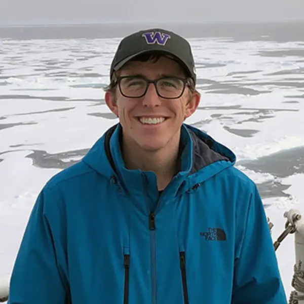 A person smiles at the camera with glaciers in the background.
