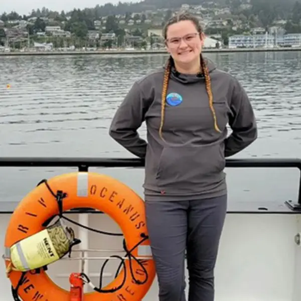 A person stands beside a life ring on a boat and smiles at the camera.