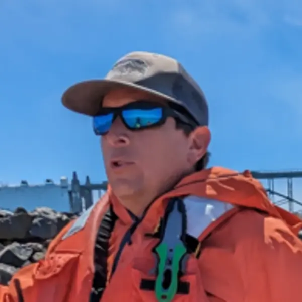 A man wearing boating safety vest, baseball hat and sunglasses.