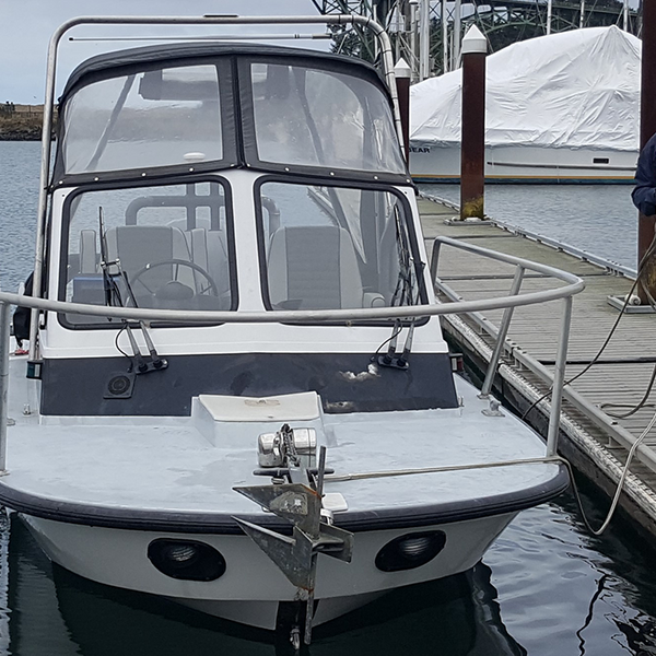 A small fiberglass boat with a soft cabin cover is being tied to a pier by a person in a lifevest.