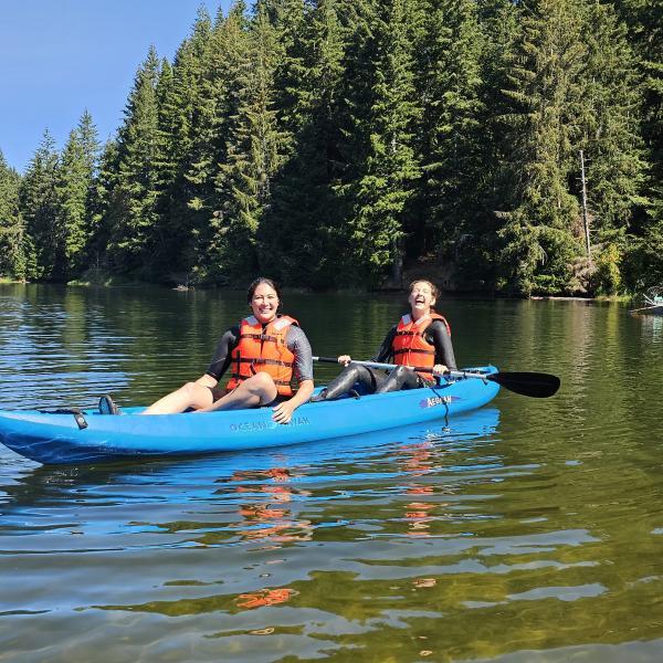 Two people wearing lifevests sit in a blue inflatable kayack.